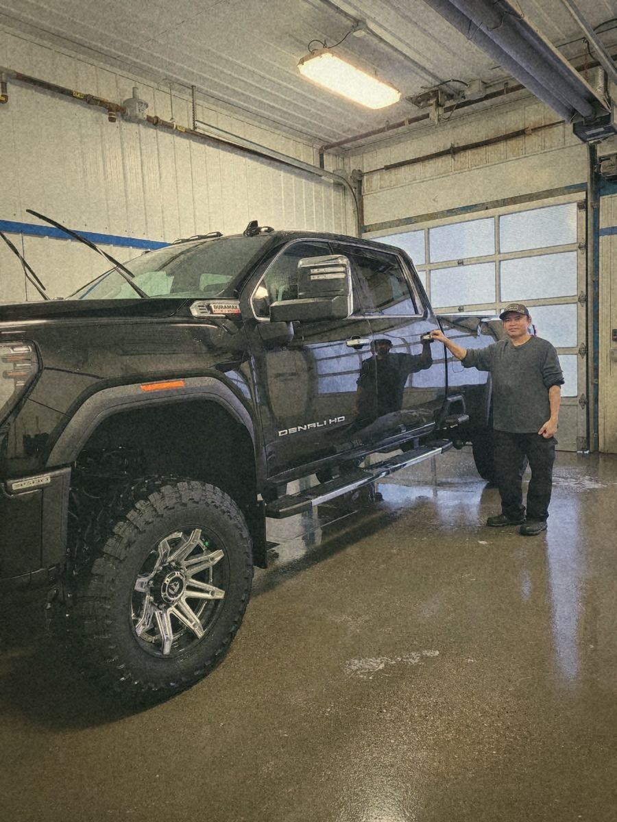 Junior standing beside a freshly detailed black pickup truck in the wash bay