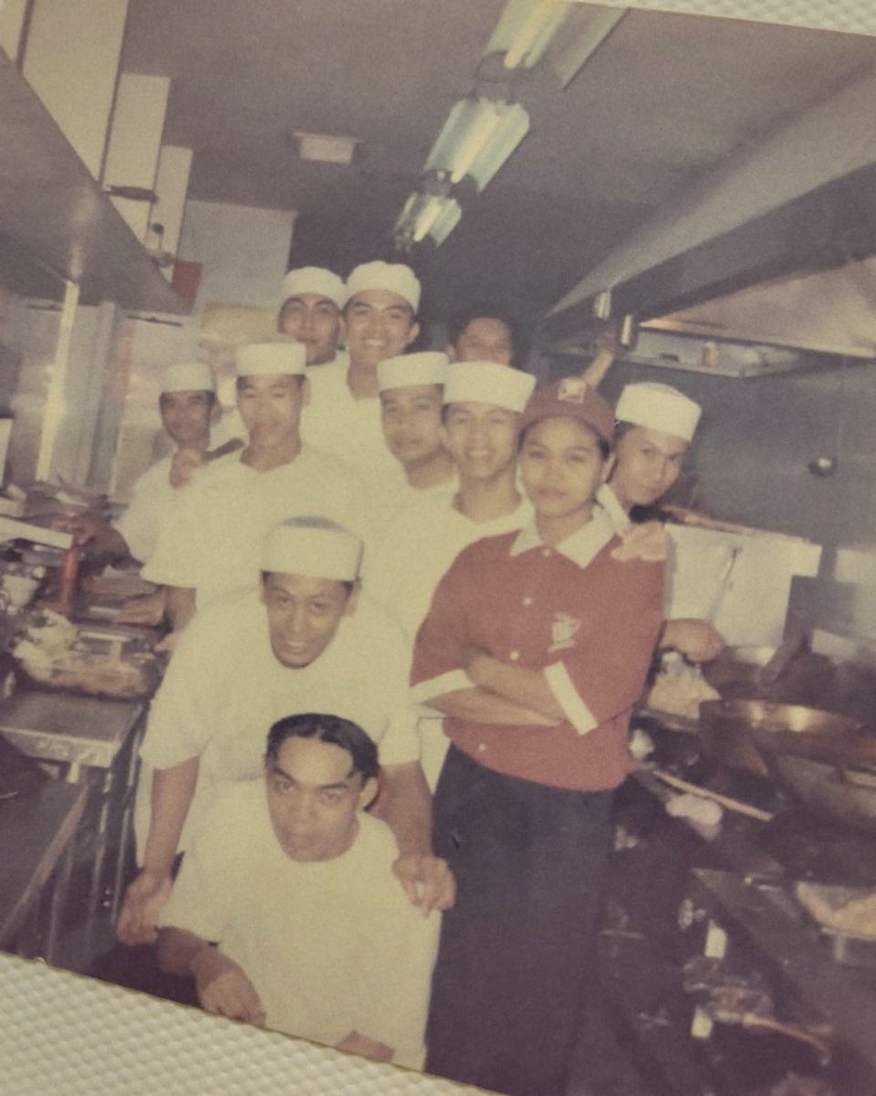 A kitchen crew in white caps posing together in an old restaurant kitchen